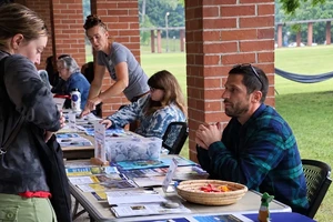 People look at tables promoting different campus activities. On one table is a basket of candy and a tub of small, flat rocks.