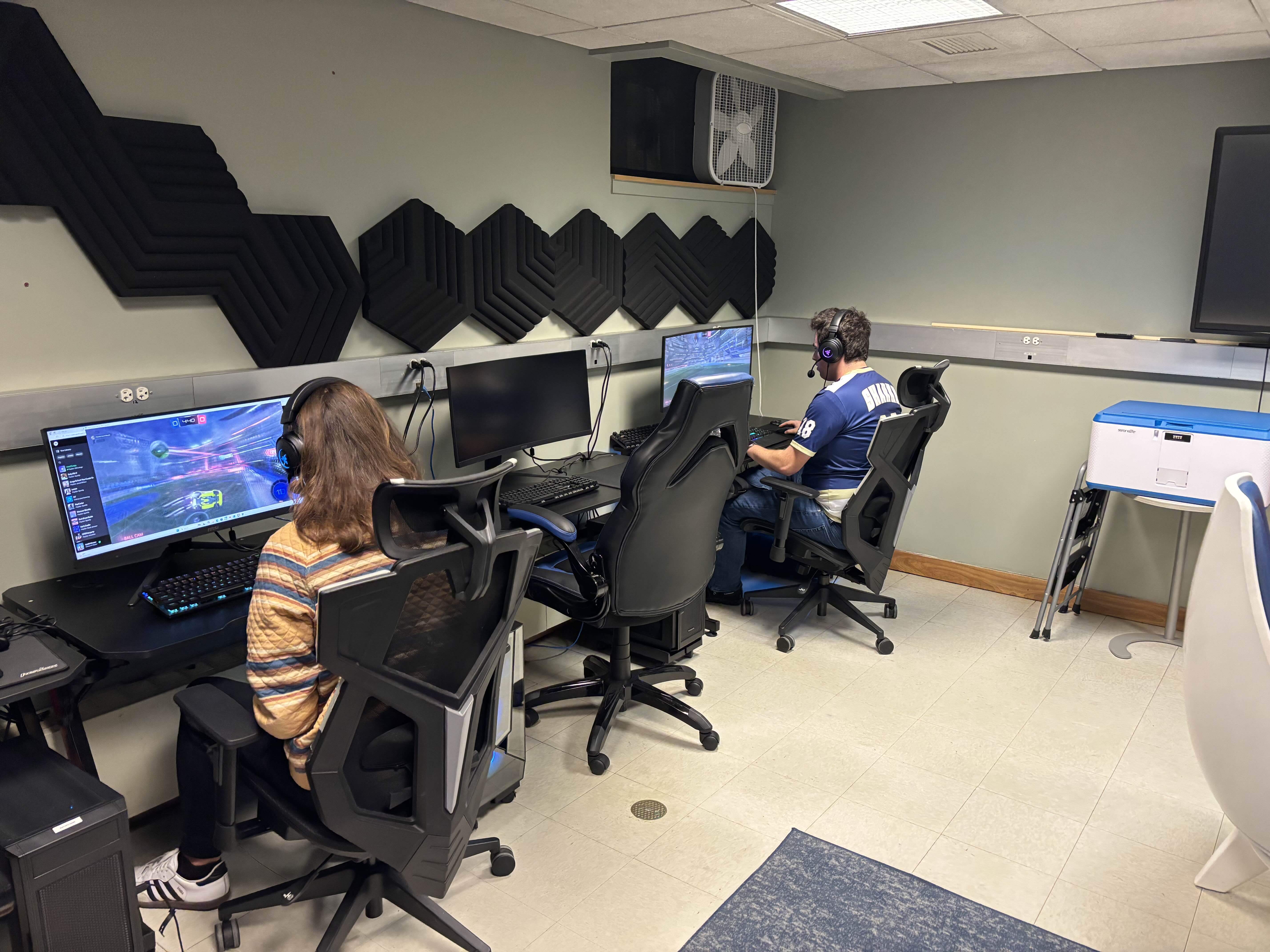 Gamers competing in an online competition, sitting in front of computers in a room with decorative black sound-proofing wall tiles.
