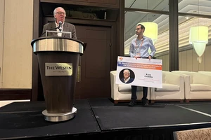 Ken Gobbo giving a speech with a presenter holding the award to the right of the podium.