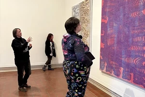 Student looking at large colorful artwork on a gallery wall with a woman standing behind her and gesturing in explanation.