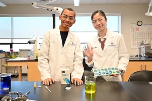 Two Landmark College students in dresses in white coats in one of the chemistry labs on campus.