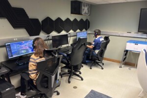 Gamers competing in an online competition, sitting in front of computers in a room with decorative black sound-proofing wall tiles.