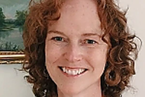 Lynne Shea facing the camera smiling with her red wavy hair and light complexion.