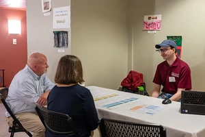 Three people talk across a table with papers scattered in front of them.