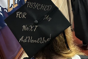 The top of a black graduation cap with Psyched for my next adventure written in gold.