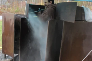 Man power washing large steel sculpture.
