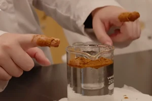 Close-up on two hands with index fingers covered in cinnamon and a large beaker of water on a table
