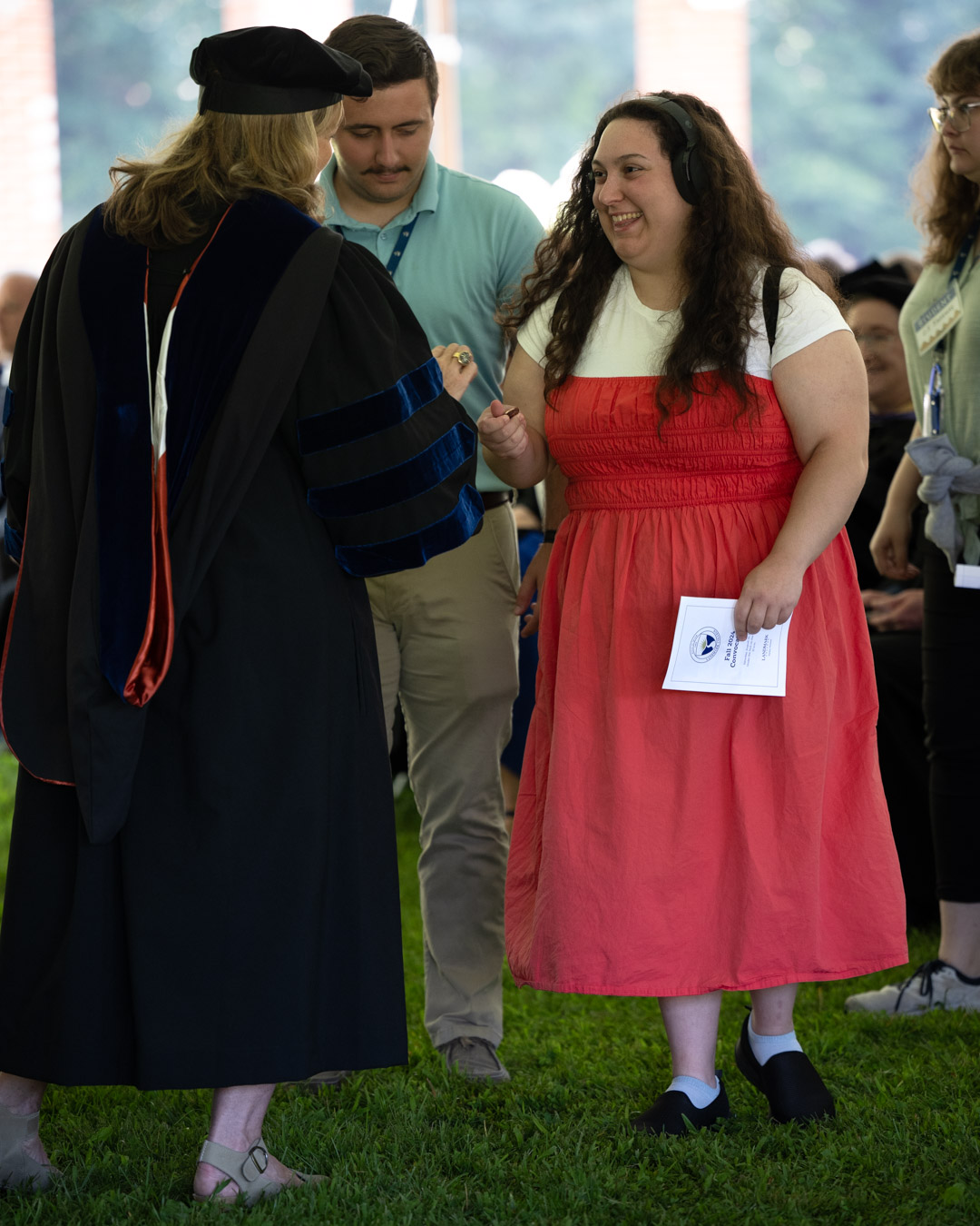A professor handing a smiling student in a red dress a coin