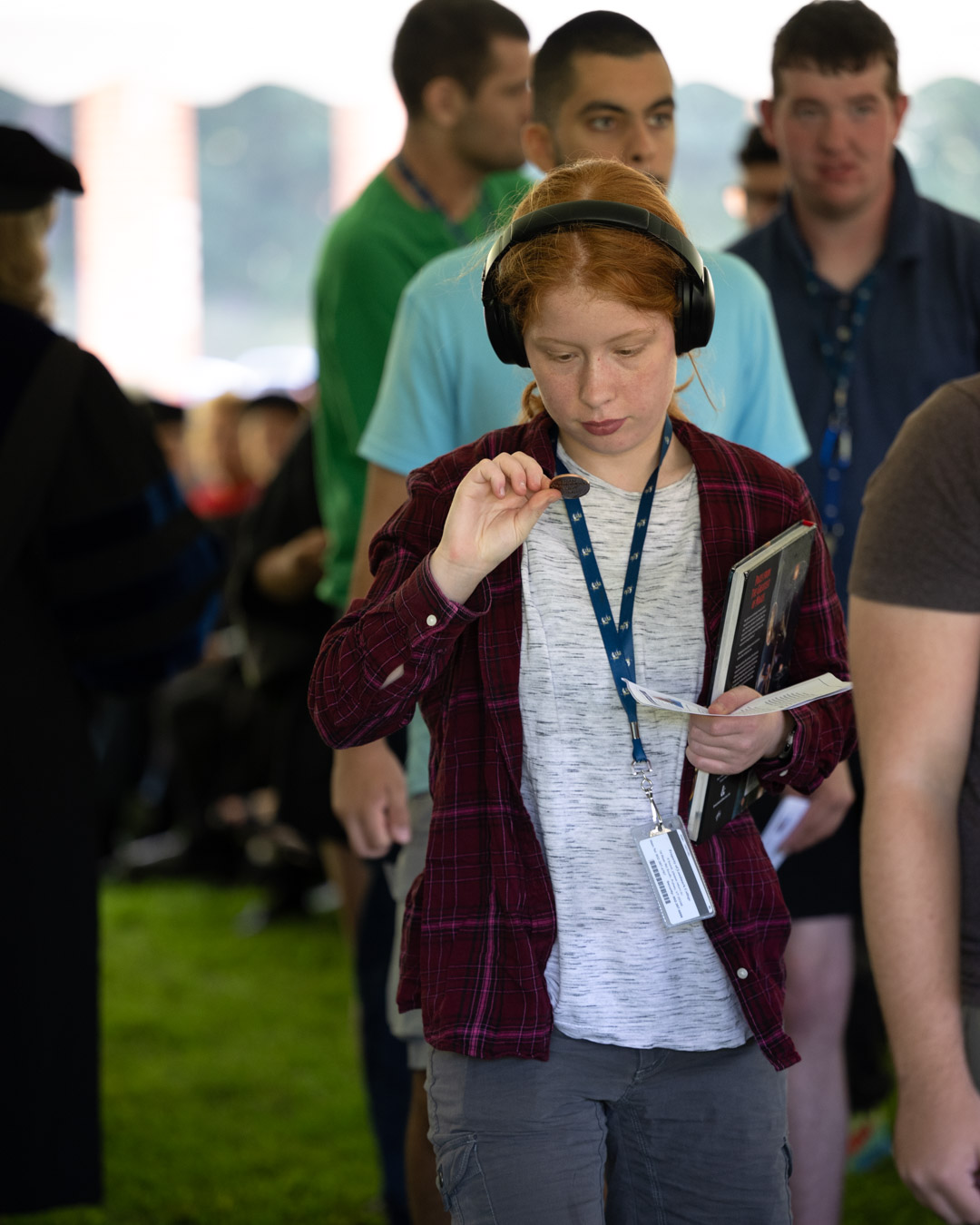 A red-headed student wearing a headset staring closely at a coin