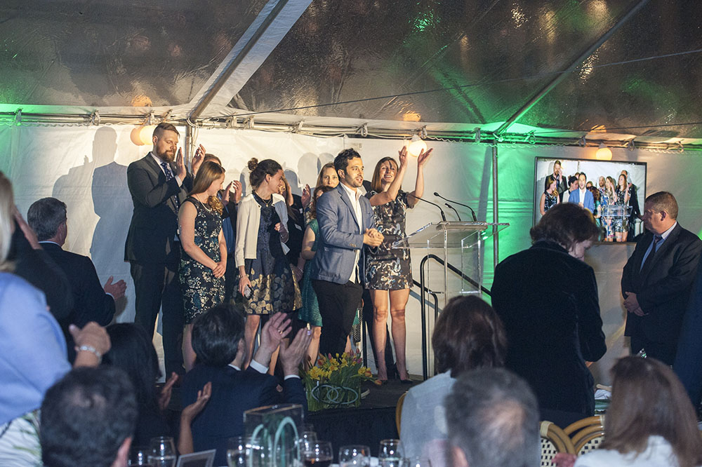Group of eight gala attendees standing at the podium in front of a clapping audience.