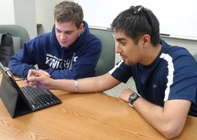 Two students interacting with a tablet on a table.