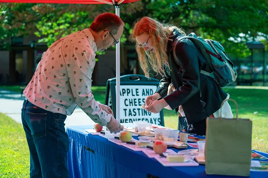 Two people discussing samples at an outdoor apple and cheese tasting booth.