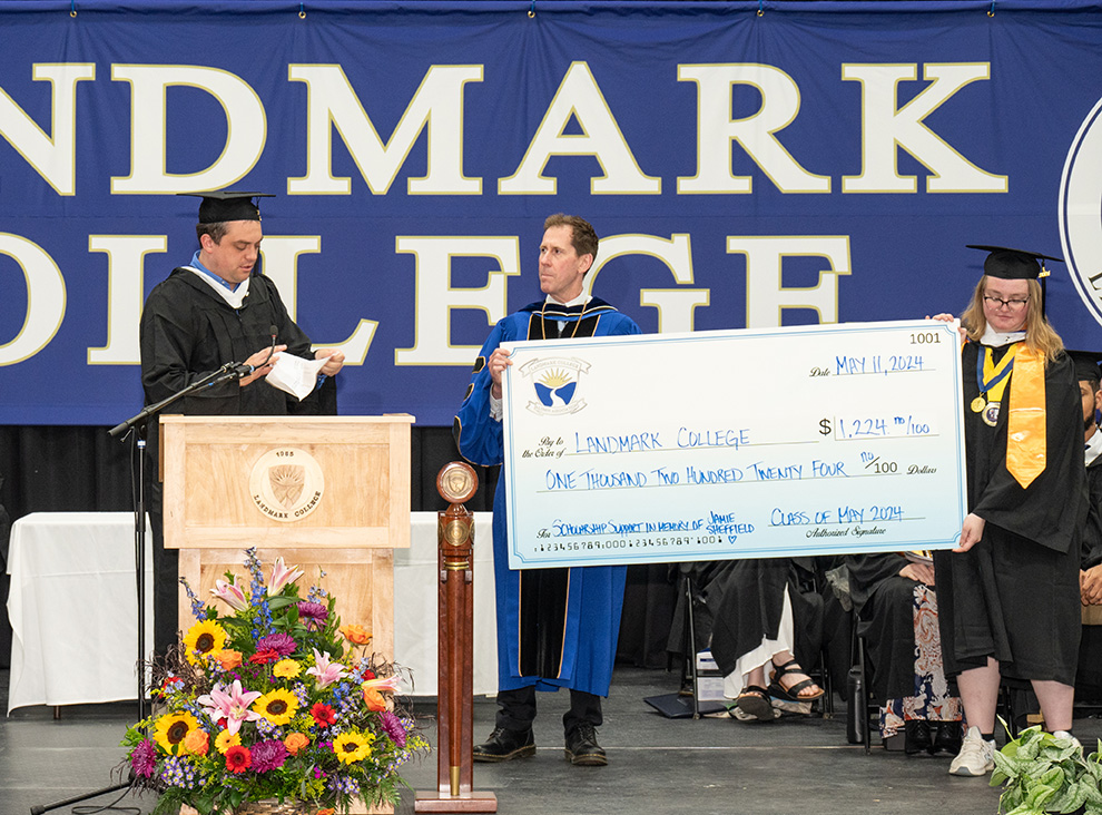 Student PJ Dudinetz at podium making remarks while President Peter Eden and student Eden Kayser hold oversized check