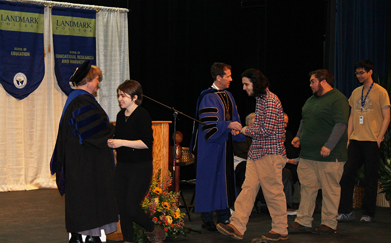 New students proceed across stage to receive coin from Landmark College president Dr. Peter Eden and Vice President of Academic Affairs Gail Gibson Sheffield during 2019 Convocation.