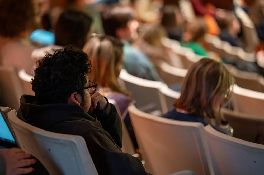 A person sits in theater-style seating while watching a presentation.
