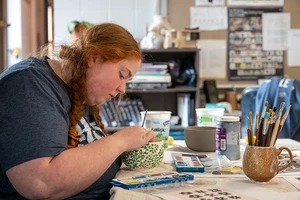 A person decorates a bowl with designs of leaves and vines on the outside.