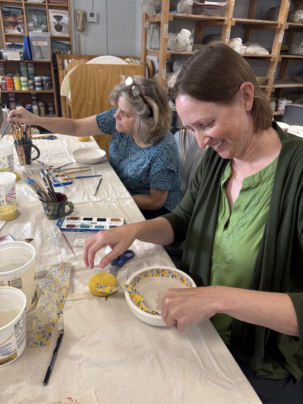 Two people design bowls while sitting at a table.