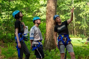 Three people, wearing helmets, stand outdoors at a ropes course.