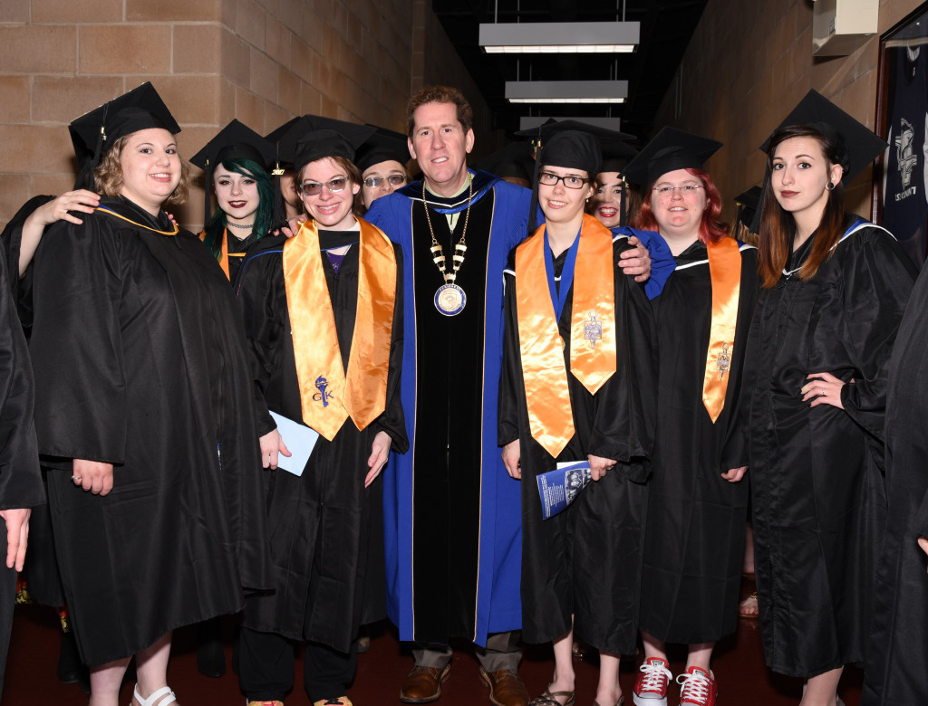 Graduates in academic regalia in the Click Family Sports Center with Peter Eden.
