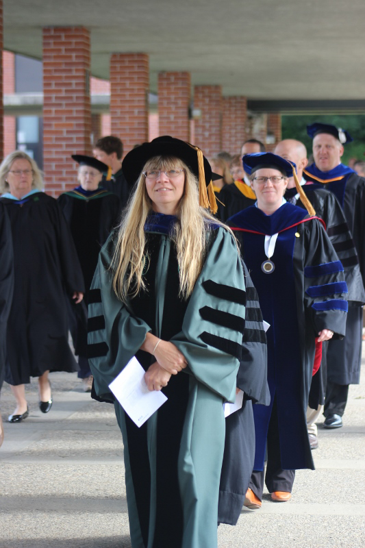Faculty member in black cap and robe leads row of robed faculty through Landmark College colonnade.