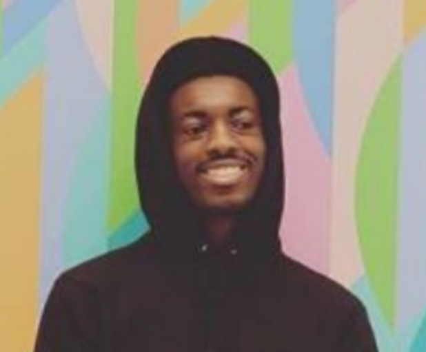 Julius Udochi standing in front of a colorful background, wearing a black sweatshirt with the hood pulled up.