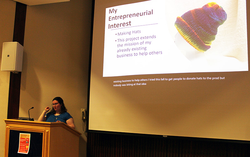 Female student at podium with presentation slide on projector behind her.