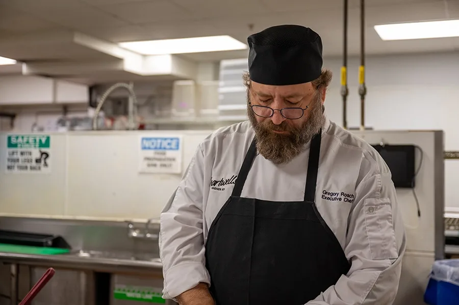 A chef dices onions in an industrial kitchen, looking at his hands as he works.
