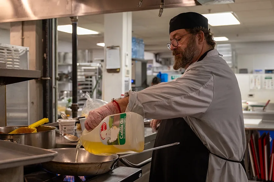 A chef pours oil into a pan in an industrial kitchen.