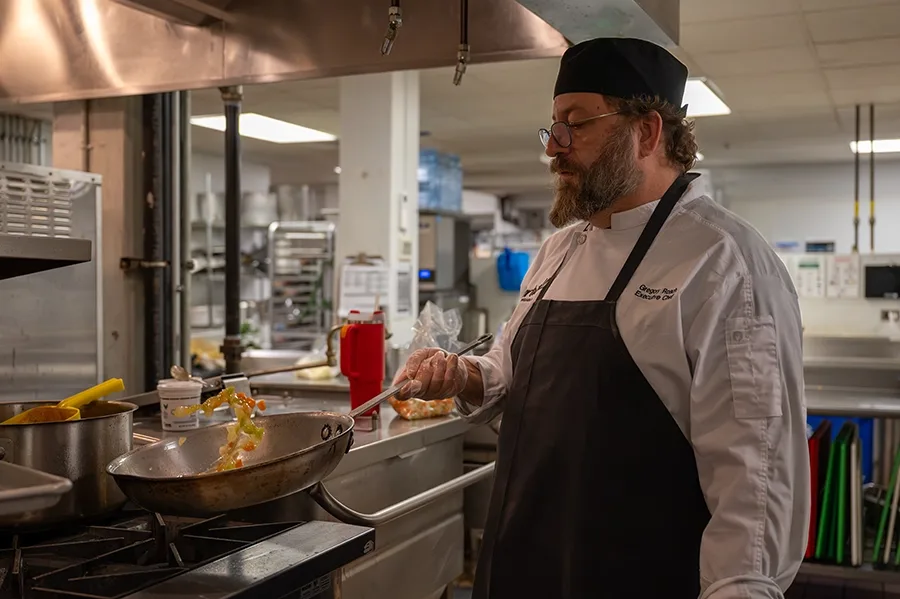 A chef tosses vegetables in a frying pan in an industrial kitchen.