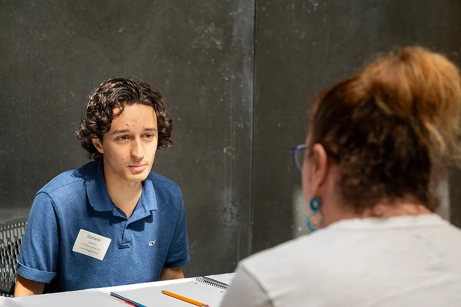 An over-the-shoulder shot of two people talking across a table.