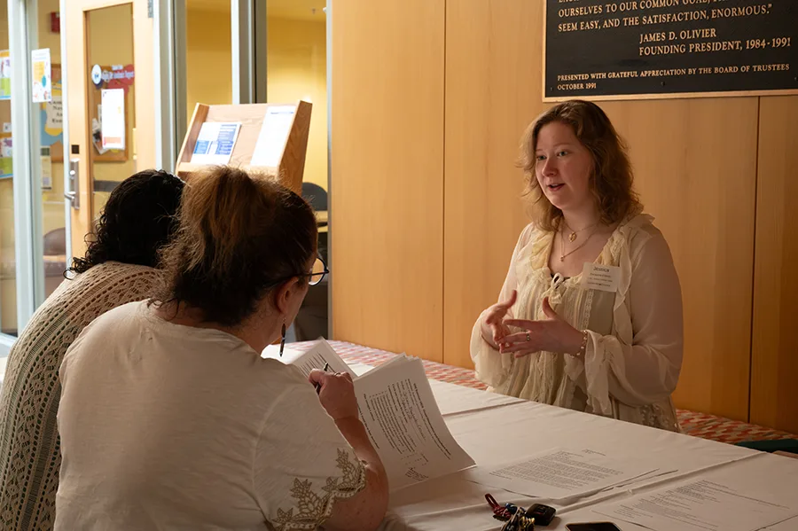 Three people talk across a table with papers scattered in front of them.