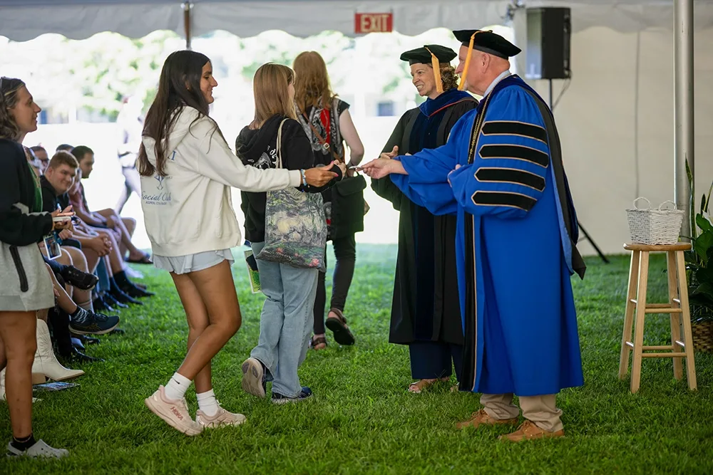 A person is handed a coin by a college president.