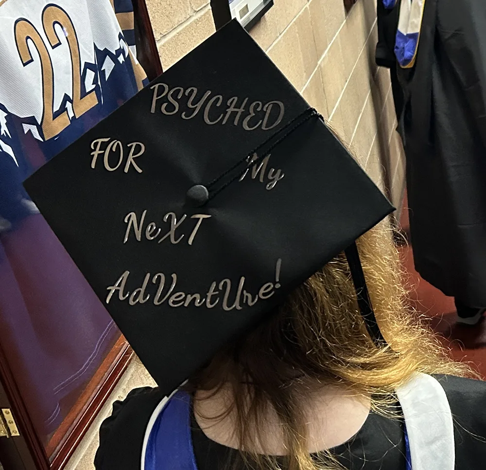 The top of a black graduation cap with Psyched for my next adventure written in gold.