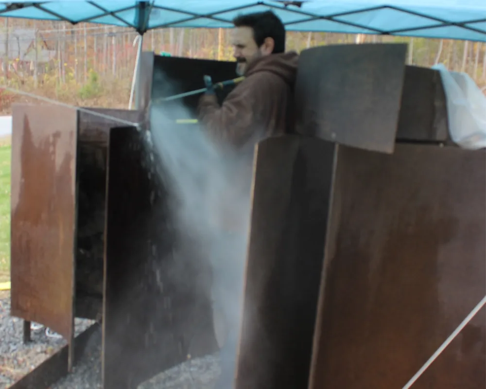 Man power washing large steel sculpture.