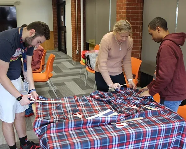 Two student and an instructor measuring and cutting fabric