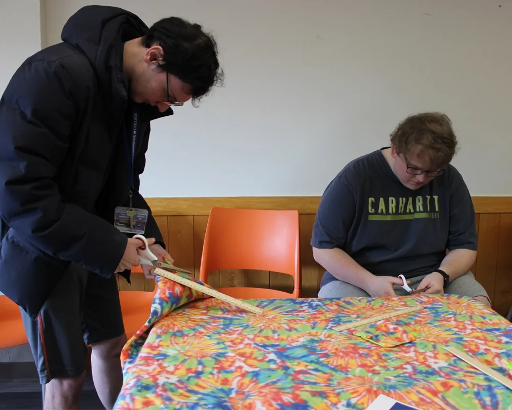2 mail students measuring and cutting a tie dye patterned fabric