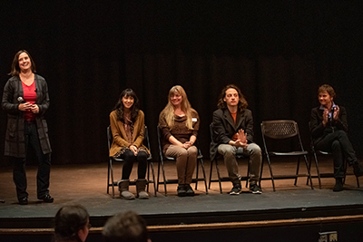NIH panel members sitting in foldable chairs on stage, with one person standing.