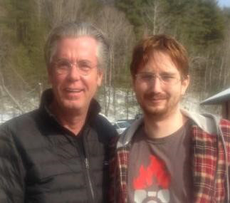 Two men standing side-by-side smiling at the camera outdoors.