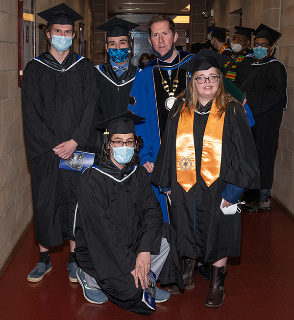 President Peter Eden posing with group of students in graduation caps and gowns before December 2021 Commencement ceremony.