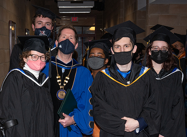 President Peter Eden posing with group of students in graduation caps and gowns before December 2021 Commencement ceremony.