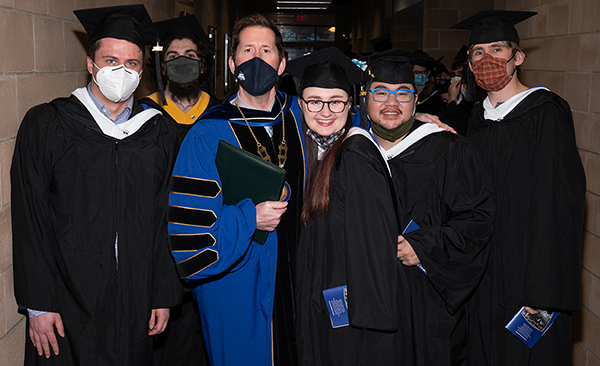 President Peter Eden posing with group of students in graduation caps and gowns before December 2021 Commencement ceremony.
