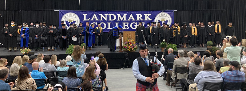 A picture of the stage at Commencement after all the graduating students and faculty have filed in. They are still standing as the bagpipe player who led the procession walks away down the center aisle.