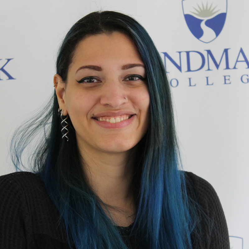 Image of woman with black hair with blue streaks facing camera and smiling.