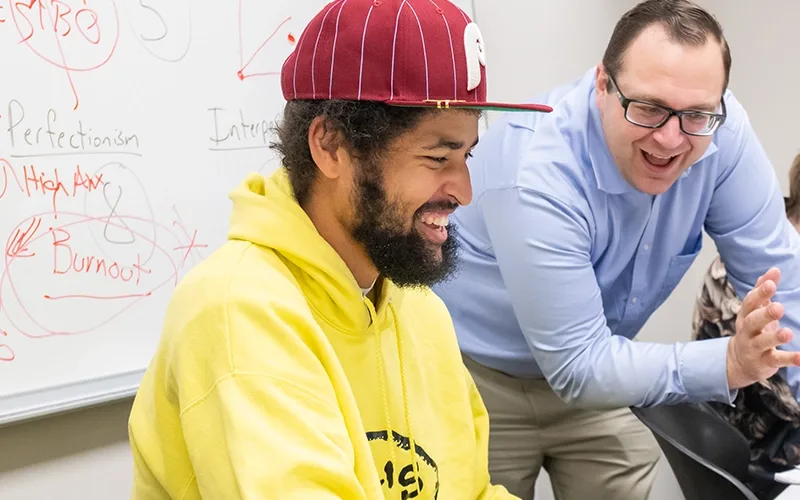 Adam Lalor, right, in a very light blue shirt, supports a Landmark College student, in a yellow sweatshirt and red hat, in an independent research project.