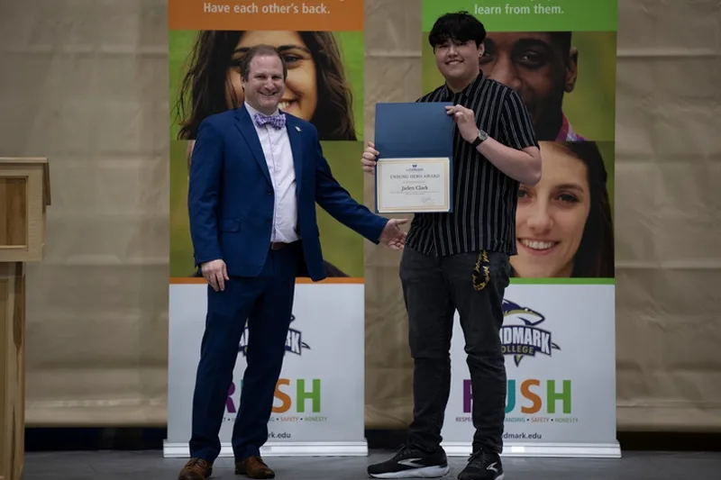 A student holding his award next to the Dean of Students and Director of Student Engagement.