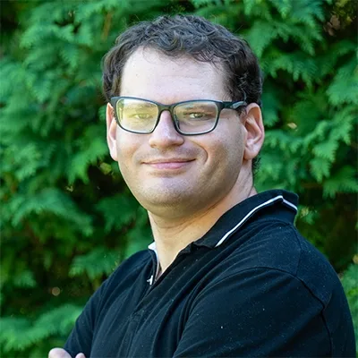 A headshot of Gus Zarefsky in front of arborvitae.