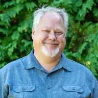 A headshot of Andrew Wilcox in front of arborvitae. 