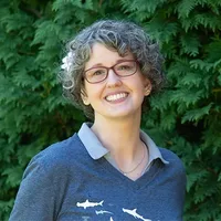 A headshot of Daisy Milman in front of arborvitae. 