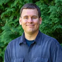 A headshot of Heath Bailey in front of arborvitae. 