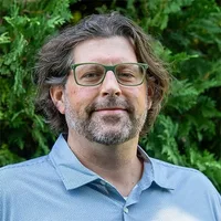 A headshot of Jim Kraly in front of arborvitae. 